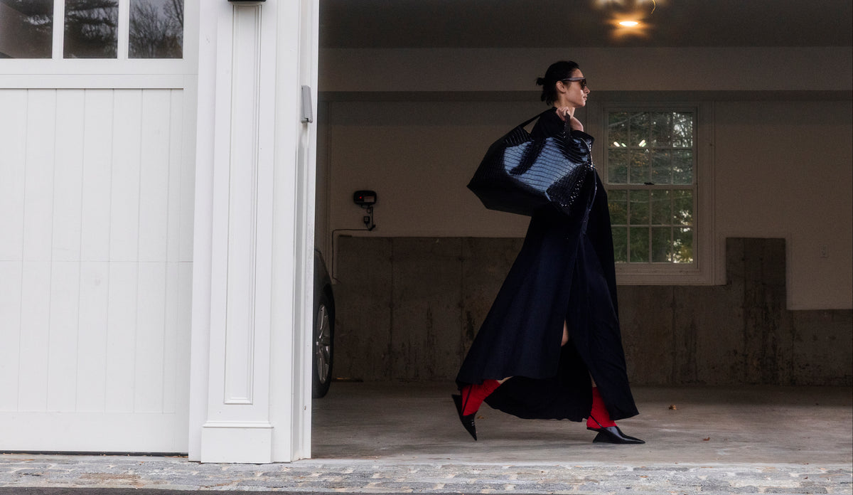 Woman walking in a garage carrying the LA MAMA LM1 luxury handbag in Black Lacquer Croco in her hand.
