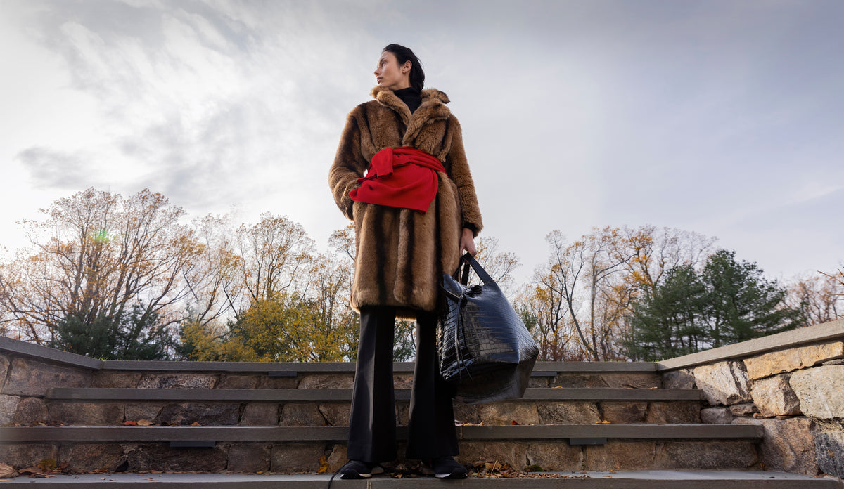 Woman standing on steps carrying the LA MAMA LM1 luxury handbag in Black Lacquer Croco in her hand.