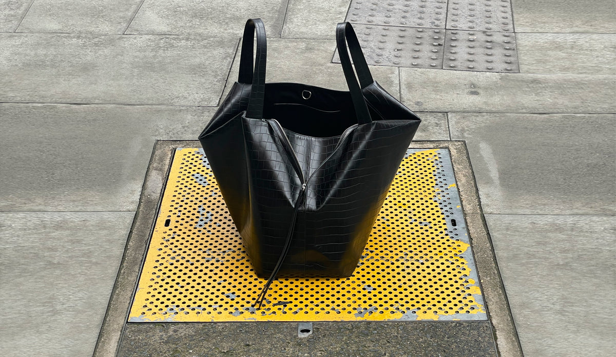 LA MAMA LM1 luxury handbag in Black Matte Croco on the street on top of a yellow grate.