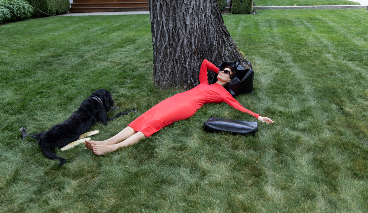 Woman in a red dress lying on a lawn with the LA MAMA LM1 handbag and XL Pouch in Black Matte Croco on the floor.