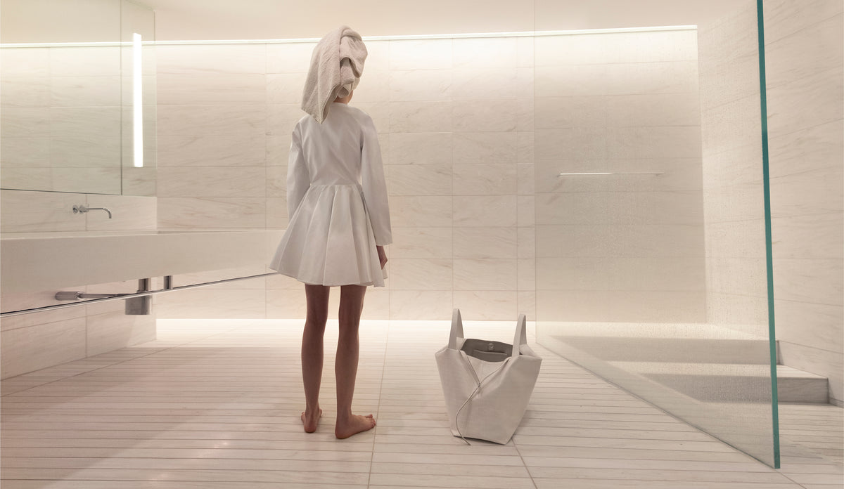Woman standing in a modern bathroom with the LA MAMA LM1 luxury handbag in White Matte Croco on the floor.