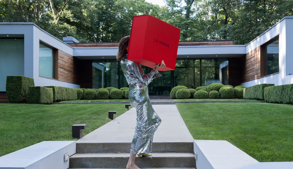 Woman standing in front of a modern house carrying the LA MAMA red box.