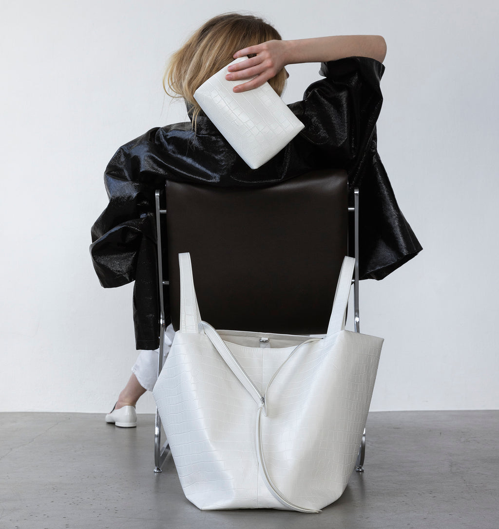 Model carrying the Small Pouch in White Matte Croco in hand with the LA MAMA LM1 handbag in White Matte Croco on the floor.